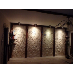 Kamień dekoracyjny ułożony w pokoju między filarami z drewna.